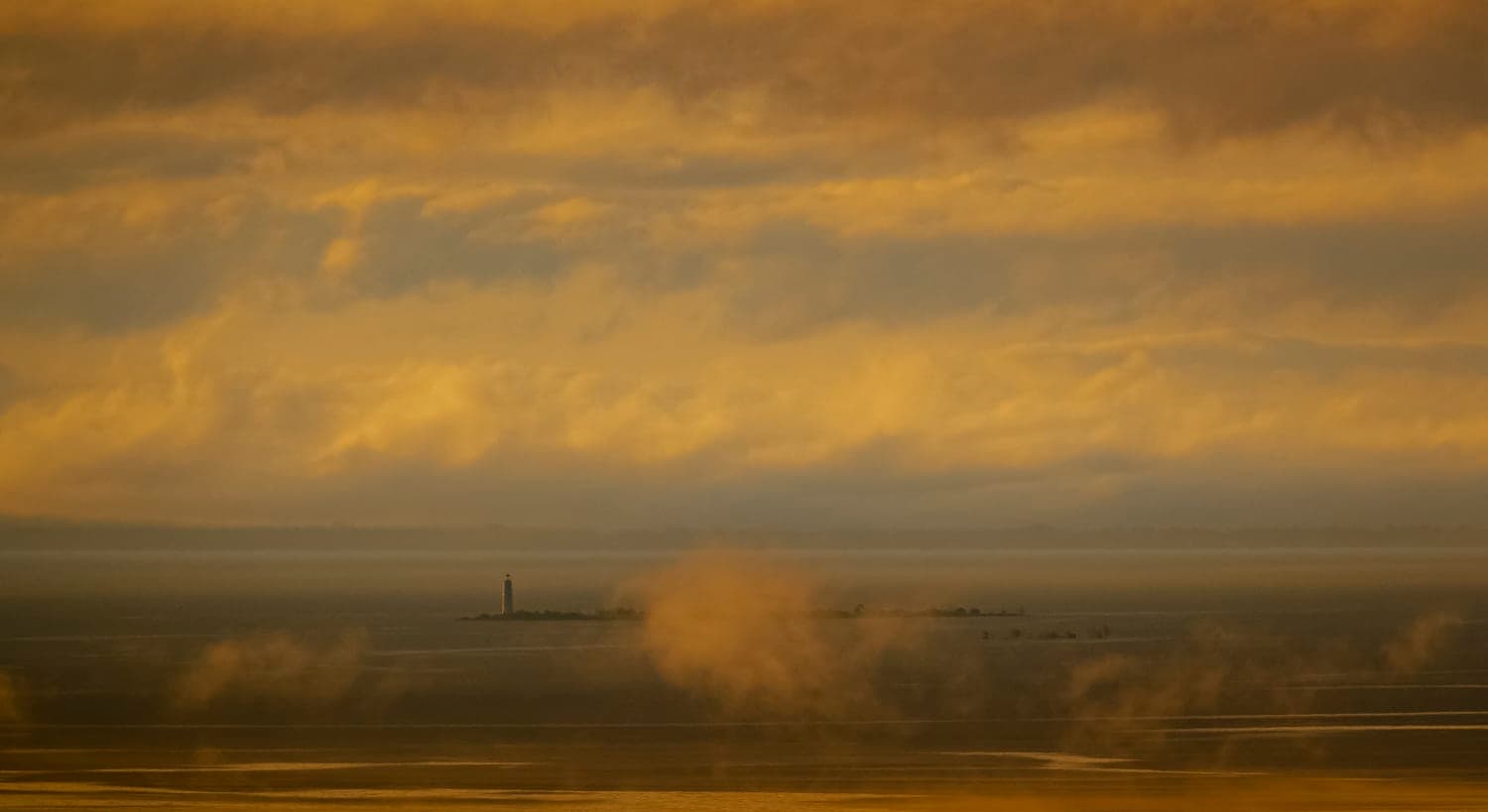 Fog and morning light over a distant lighthouse point