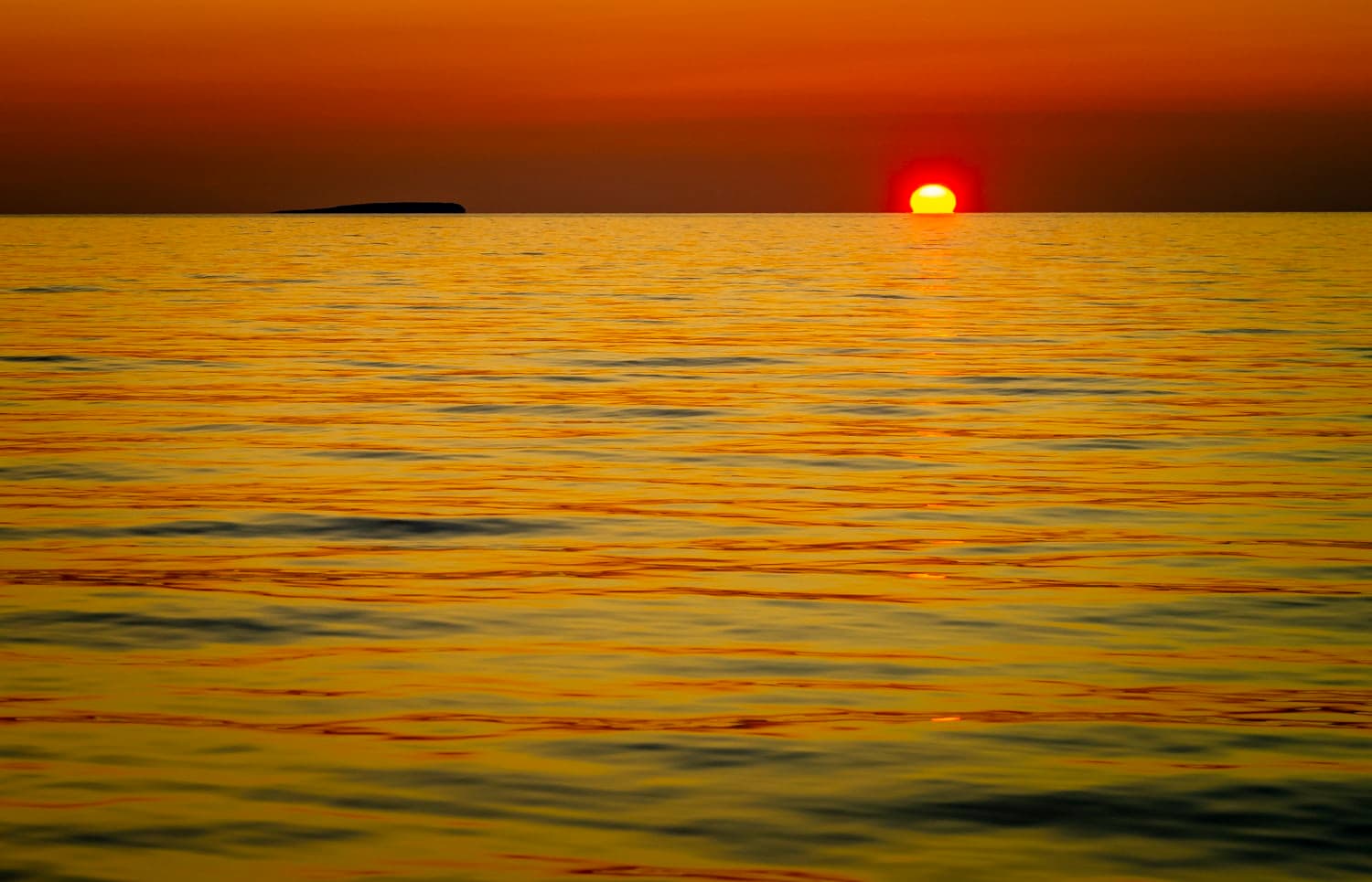 Sun setting at the horizon beside a low island