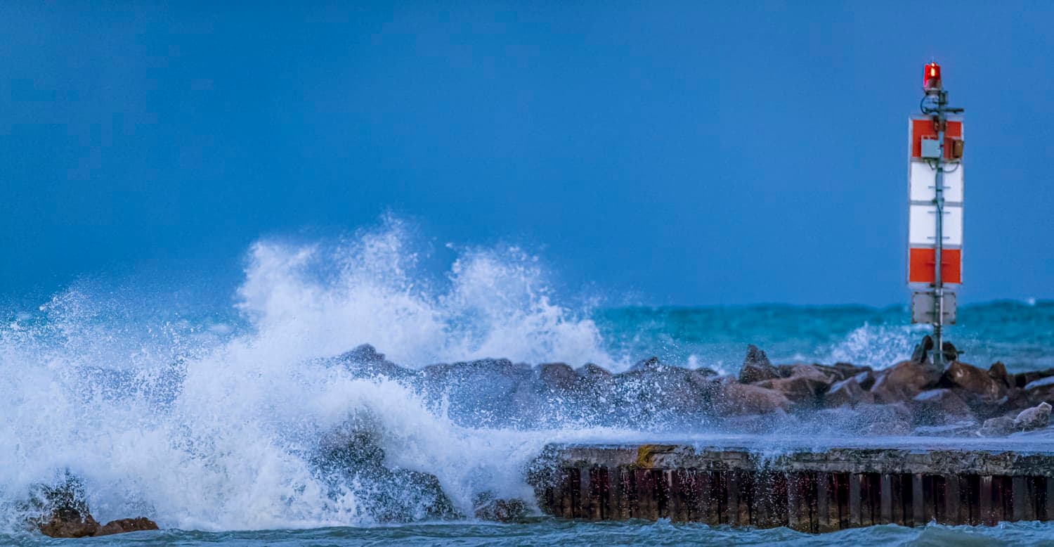 Waves breaking over a breakwater beside a channel marker