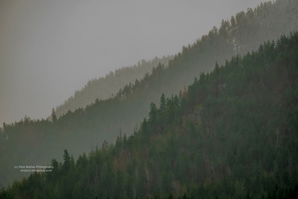 Rain sweeping across a forested escarpment ridge