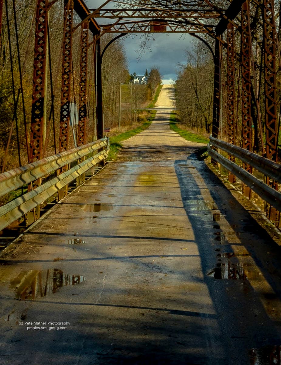 Iron truss bridge looking down a wet country road