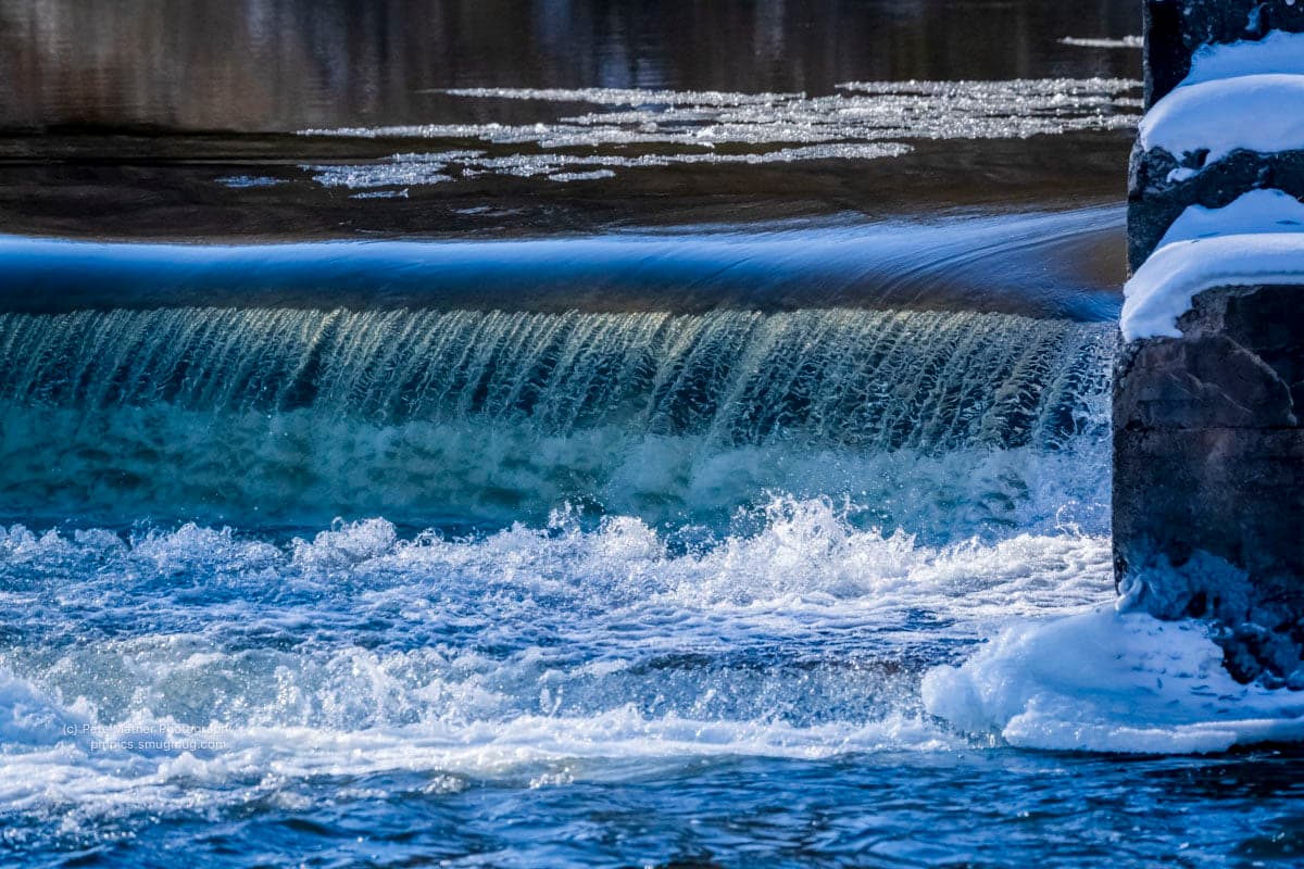 Water pouring over an ice-rimmed weir in winter