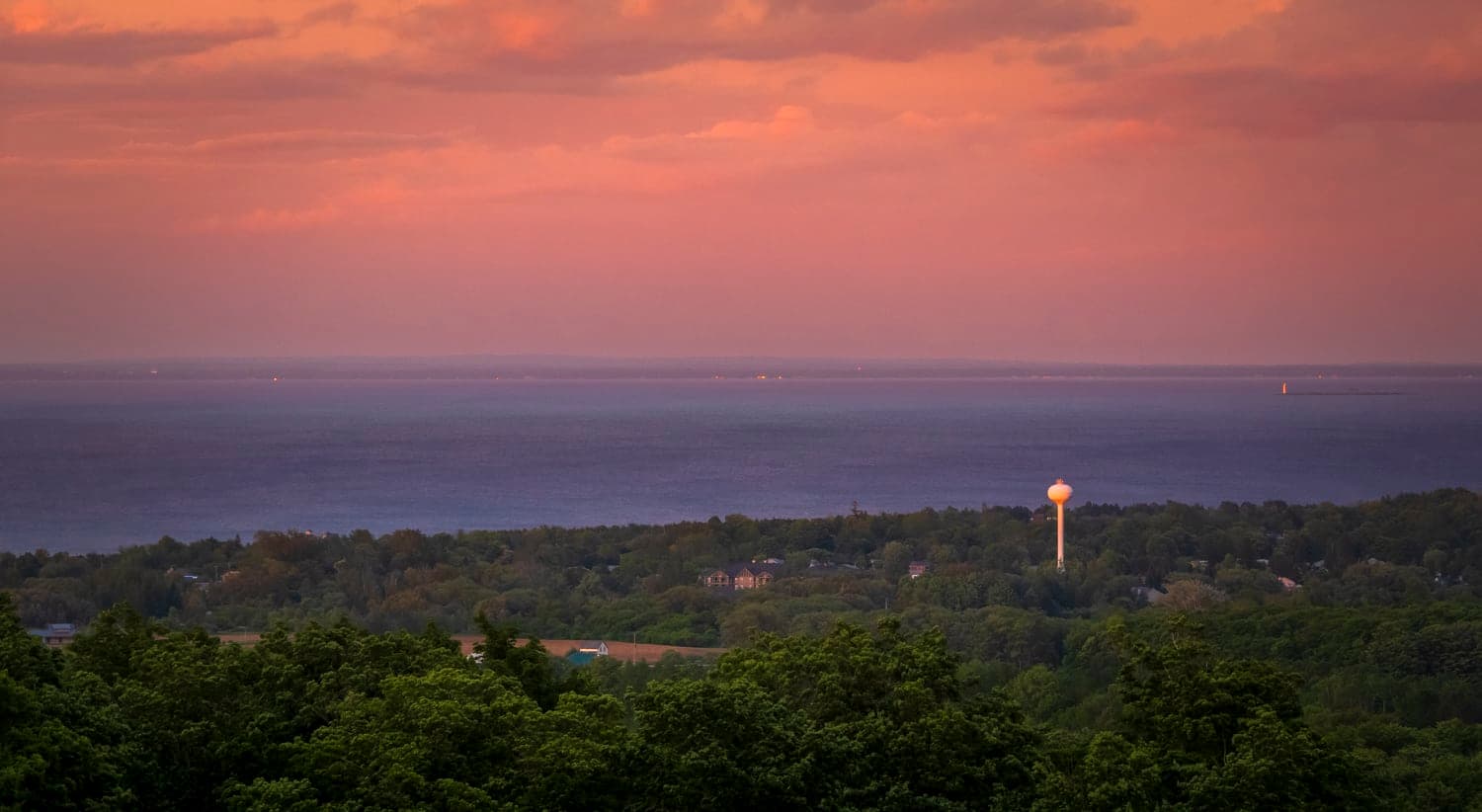 Town and water tower lit at dusk above the shoreline