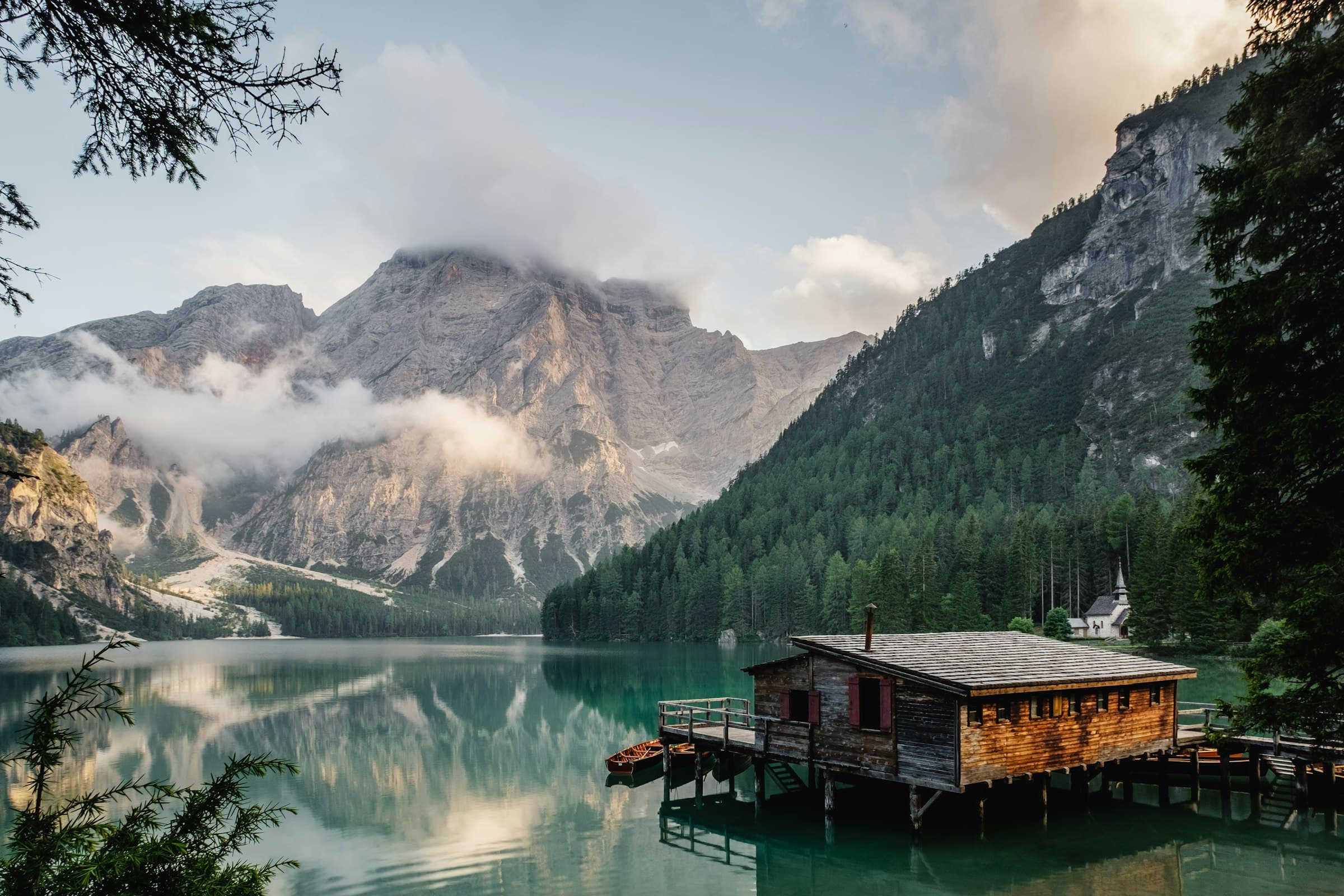 Still water and a wooden dock beneath forested hills at dusk