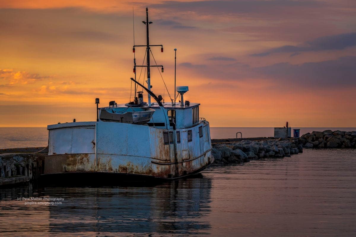 Weathered fishing boat moored at the harbour wall at sunset