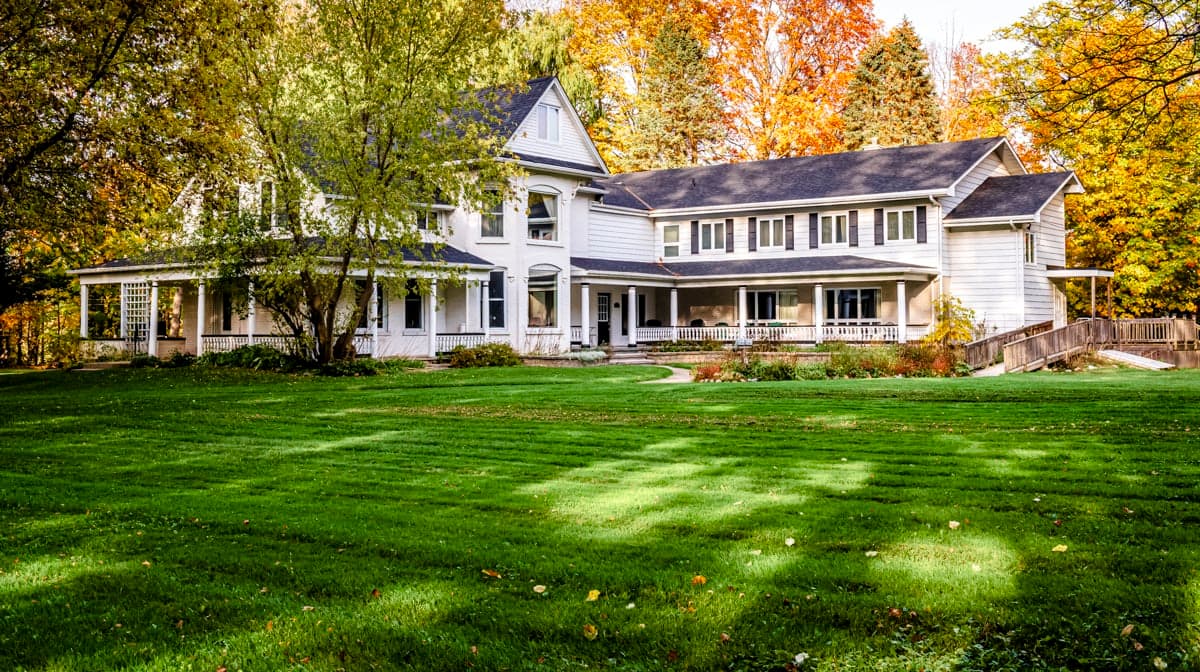 Two-storey home with wraparound porch, framed by fall colour and open lawn